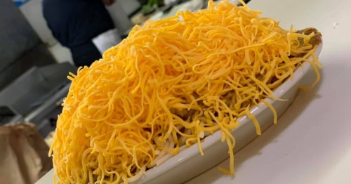 A huge mound of bright yellow shredded cheddar cheese piled high in a white dish.