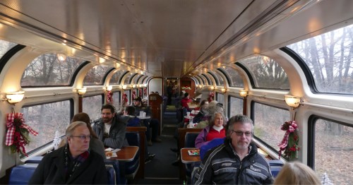 The inside of the North Pole Express train with two windows lining each side of the train and passengers seated at tables.