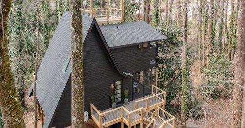 Exterior of a black, Scandinavian-inspired Airbnb treehouse surrounded by bare trees