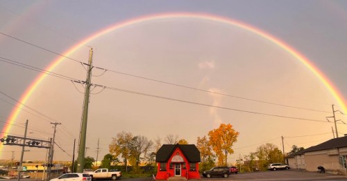 The tiny red Choo Choo Grill building is framed by a vibrant, full rainbow at sunset.