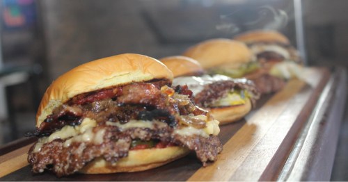Close-up of steaming hot, cheesy, bacon-loaded smash burgers and other options from Leo's restaurant. 