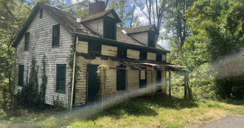 Abandoned home in near-ruins surrounded by the woods on a sunny day.