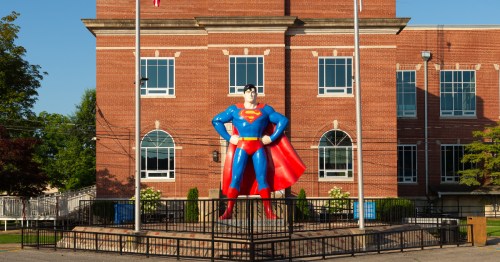 A red brick building in the background with a giant statue of Superman with his hands on his hips in the center.