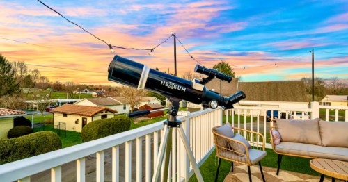 Side view of a telescope on a balcony at an Airbnb with a colorful sunset behind it