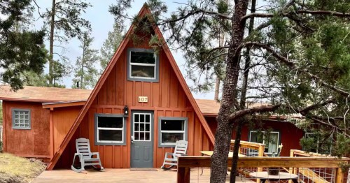 The exterior an A-fram cabin surrounded by forest.