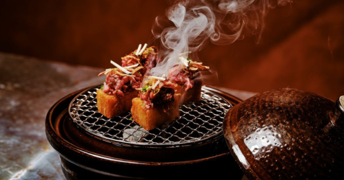 a hibachi with cubes of wagyu beef steaming from the heat cooking it from below