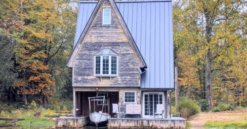 Charming, tall wooden boathouse rental built directly on a pond, surrounded by colorful autumn foliage.