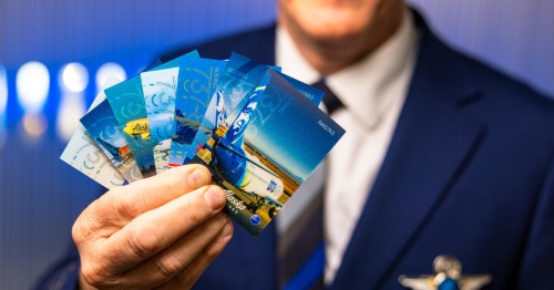 Pilot in uniform holds a fan of several blue Alaska Airlines trading cards featuring jet aircraft.