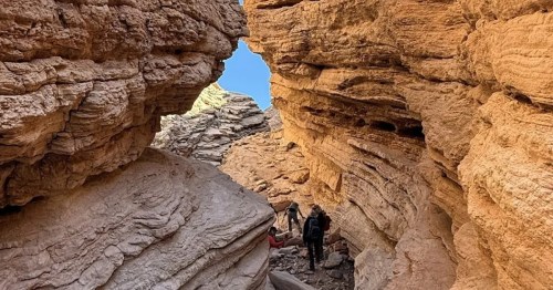 A hiker makes his way through a tight passageway between red rock canyon walls on the Anniversary Narrows Trail in Nevada.