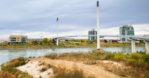 A white bridge suspended by cable over a bridge with a city building in the background.