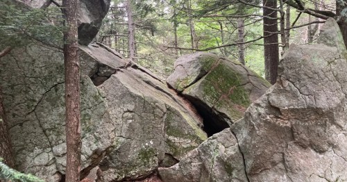 A large rock formation with a small opening to a cave.