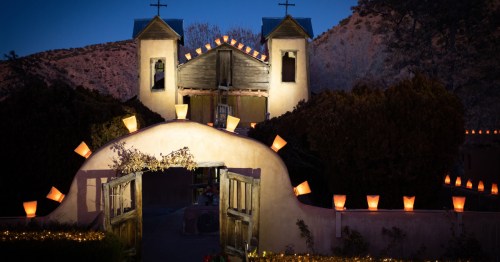 Luminarias glowing along the adobe entrance of El Santuario de Chimayó at Christmas time.