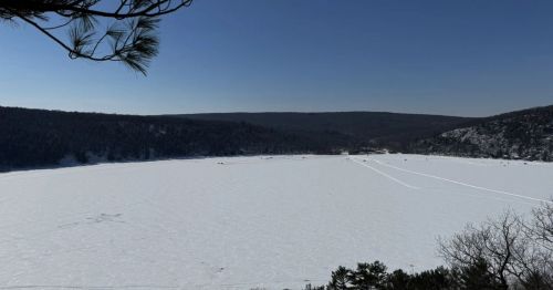 A lake covered in snow with a forest surrounding it.