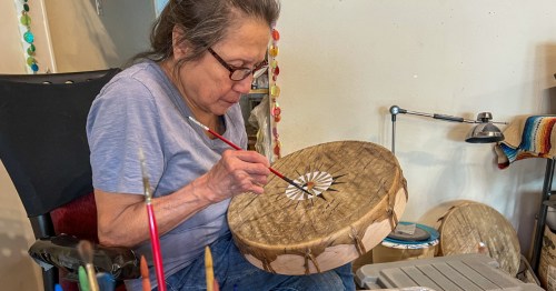 Lakota artist Sonja Holy Eagle painting the center design on a handcrafted buffalo hide drum