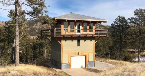 The exterior of a firetower with a garage at the bottom in a forest.