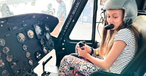 A girl sitting in the cockpit of an airplane at a museum is wearing a helmet and interacting with the controls.