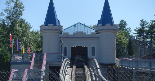 A wooden roller coaster departing from a station inside a castle.