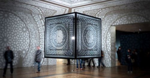 A large black cube art installation casting designs on the walls.