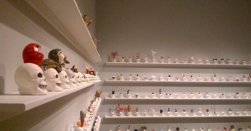 A collection of art pieces resembling skulls on a shelf against a white wall.