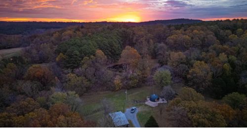 An aerial view of a glamping dome in a forest at sunset.