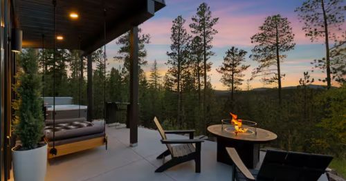An outdoor fire pit and lounge area at sunset in a forest.