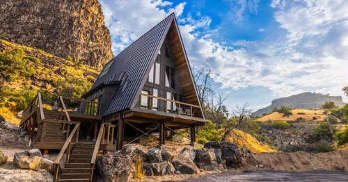 The exterior of an A-frame cabin tucked up against a rocky cliff.