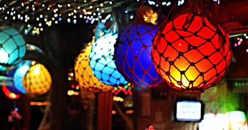 Close-up of colorful glass fishing floats wrapped in rope netting used as bright, hanging lights in a dark room.