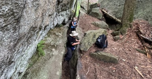 Hikers descending into the narrow, deep crevice and tight section of the famous Lemon Squeezer rock formation.