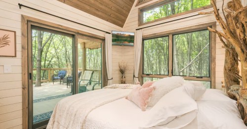 Cozy bedroom in the McHenry treehouse with white bedding, forest views, and glass doors to a deck.