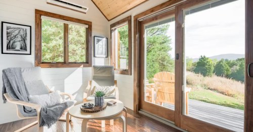 Bright living area in the tiny house with modern chairs, wood accents, and sliding door to mountain view.
