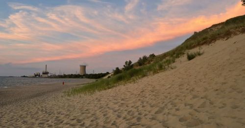 Sunset on a beach with with sand dunes and industrial equipment in the background.