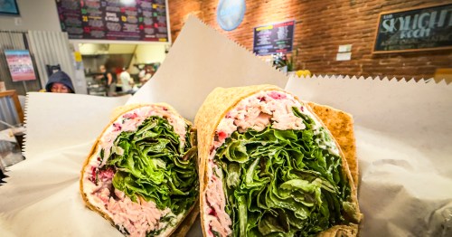 A tortilla wrap with lots of lettuce and some pink meat on the edges, wrapped in brown paper.