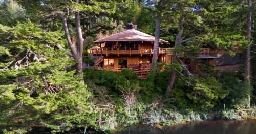 Looking across a river to an octagon-shaped home nestled in the trees.
