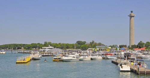Boats are docked in the water by a tall monument.