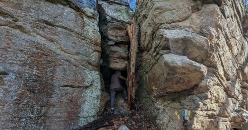 Two people entering into an extremely narrow crevasse in a rock wall.