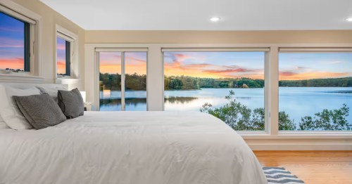 The setting sun can be seen through the large windows of the Cape Cod Lakefront Cottage Airbnb property in Sandwich, MA,