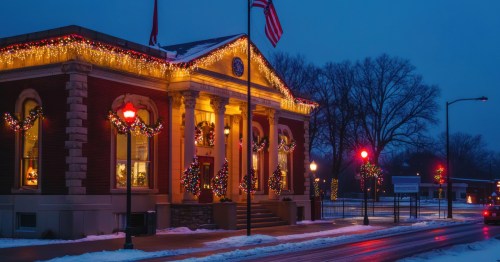 A post office is illuminated at night on a snowy street.