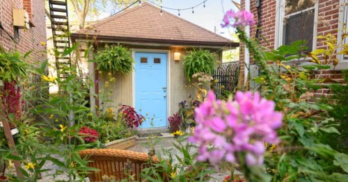 Charming Wilmington Tiny Home exterior with a blue door, lush plants, string lights, and brick buildings in Trolley Square.