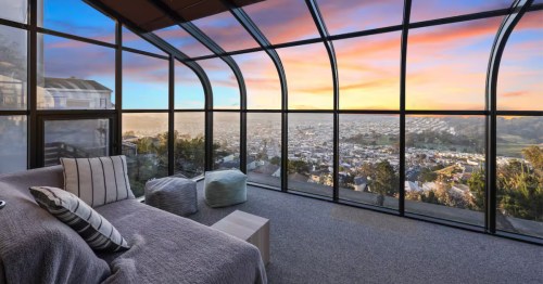 A bedroom with floor-to-ceiling windows that offers San Francisco views at sunset.