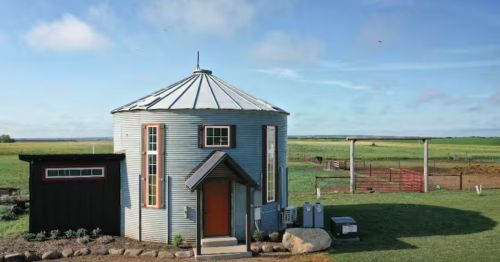 The exterior of a cylinder-shaped farm stay with a farm in the background.