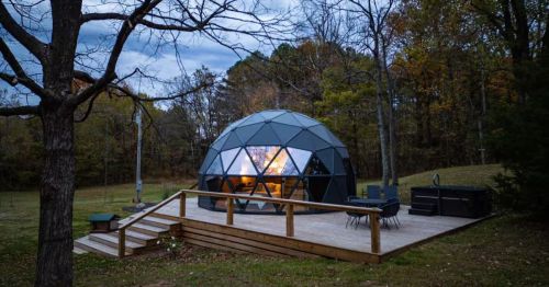 A glamping dome on a wooden deck with a hot tub set against a forest.