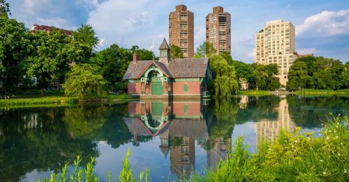 This is a ver scenic photo of the Harlem Meer, with the Charles A. Dana Discovery Center in the background. It's along the Harlem Meer walking trail, a body of water, and there's beautiful landscaping and greenery.