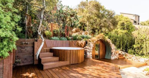 A round hillside sauna surrounded by terraced rocks and desert plants, with wooden steps leading up the landscaped slope.