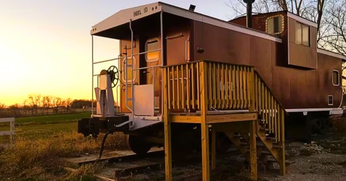 A dark red train caboose with a front porch attached for a vacational rental