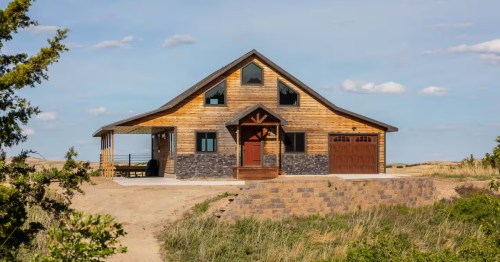 A beautiful, rustic modern barn with pale wood siding and black trim sitting on a sandy hill.