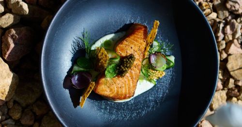 An elevated dish on a black plate on stone rocks.