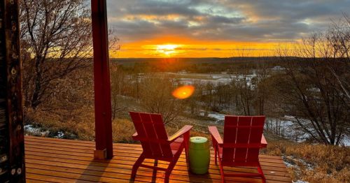 A wooden deck with two red chairs overlooking a sunset.