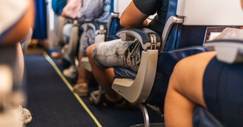 A crowded airplane aisle with passengers’ legs in shorts during flight.