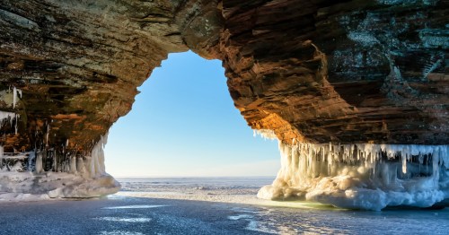 Frozen archway in the Apostle Islands National Lakeshore with a bright blue sky peeking out from inside the arch
