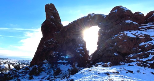 Arches National Park rock formation with winter snow and sunrise sunburst, showing the park’s peaceful off-season scenery.